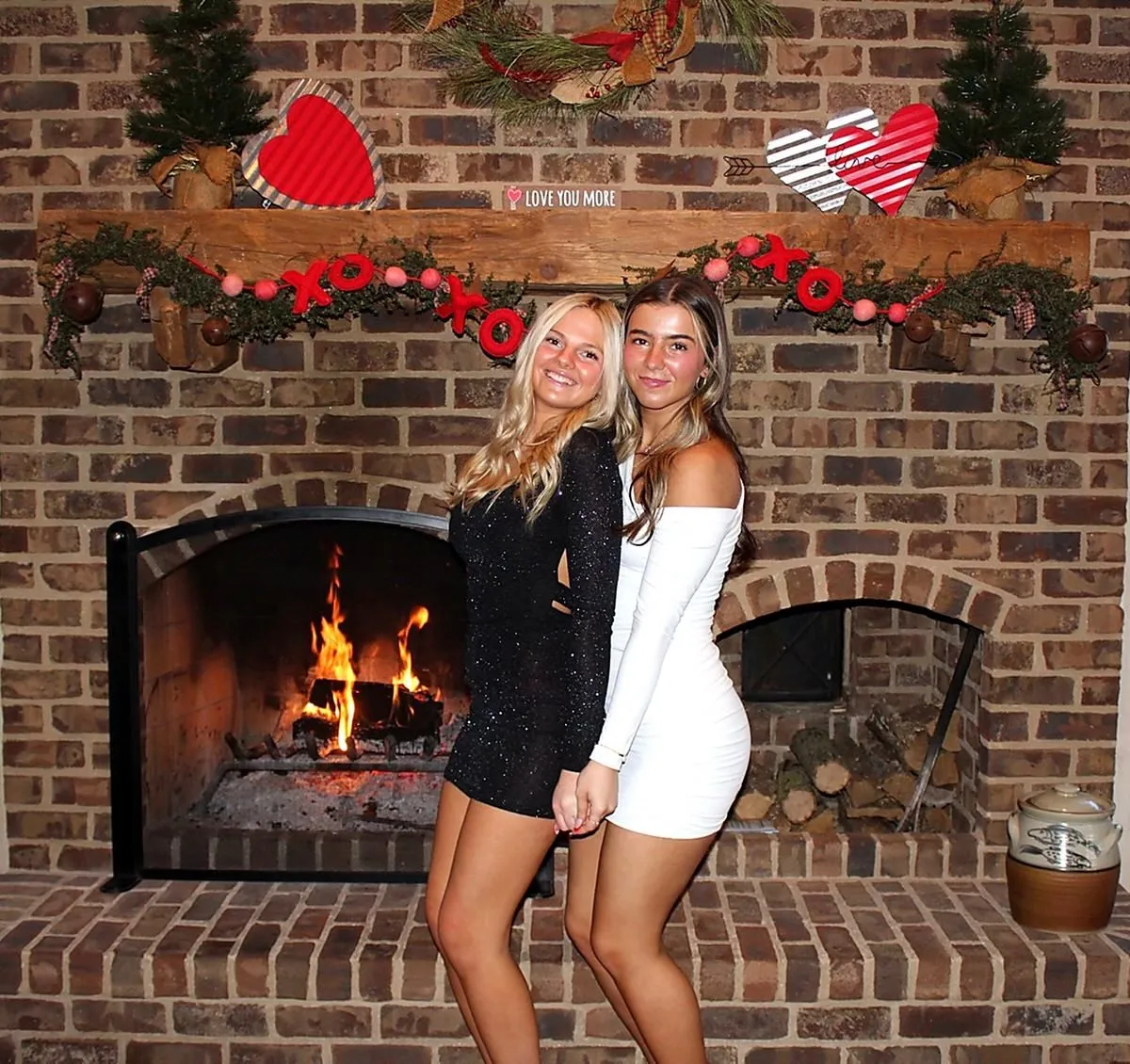 Two friends in party dresses posing by a decorated brick fireplace