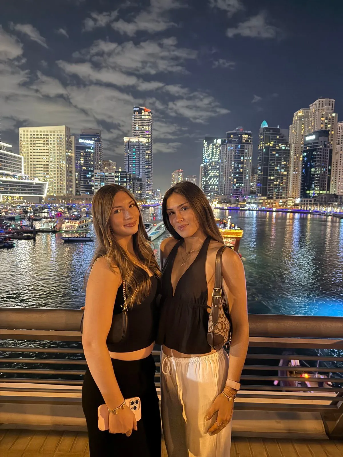 Two friends posing by the water with a city skyline lit up at night