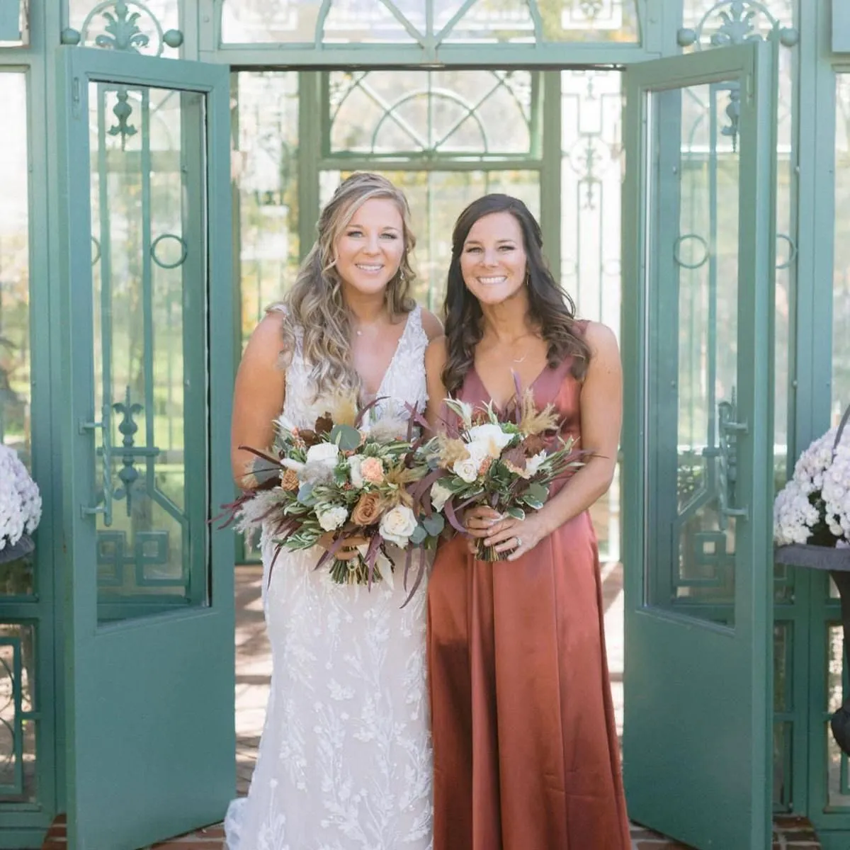 Bride and a bridesmaid in a rust dress holding bouquets in a garden doorway