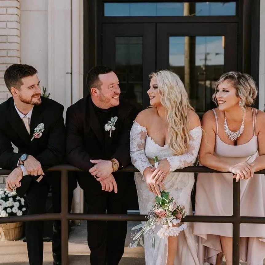 Bride and three wedding guests leaning on a railing outside a brick building