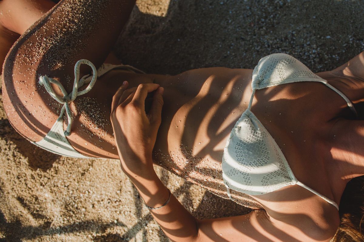 Close-up of tanned skin and a woven bikini in the sun on the sand